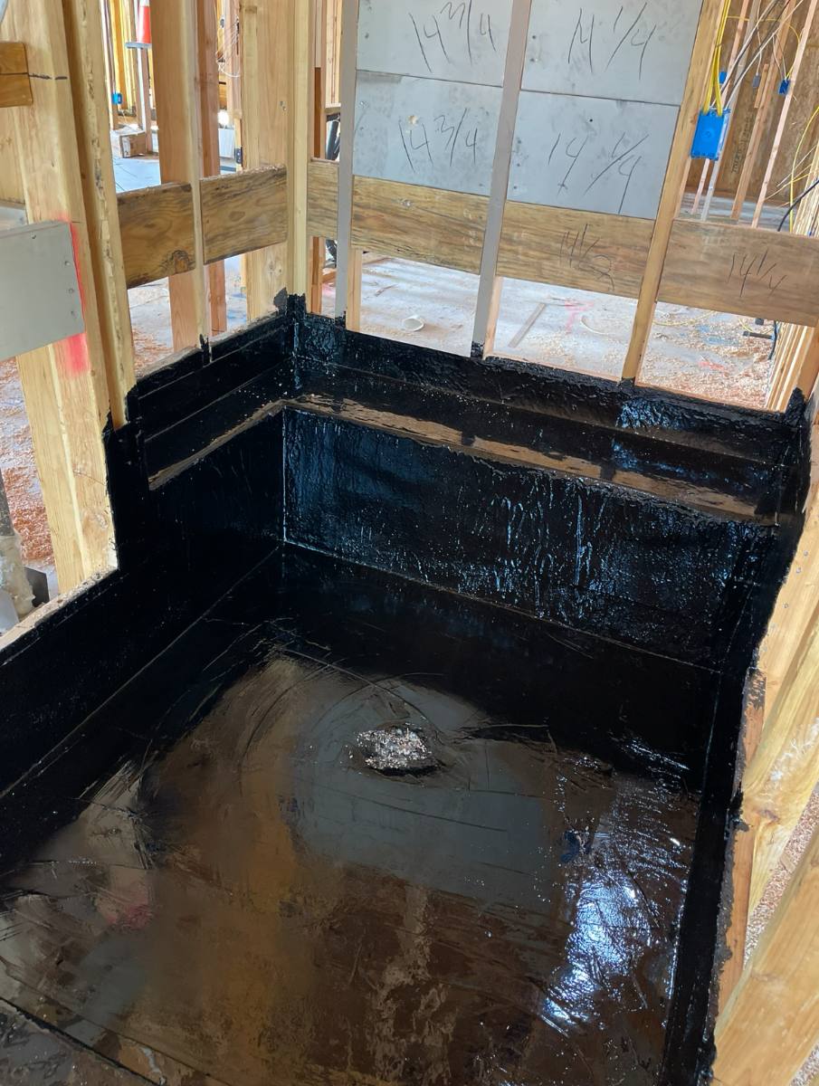 Hot mop shower pan with black asphalt waterproofing carried up the surrounding stud walls on a Sacramento job site.